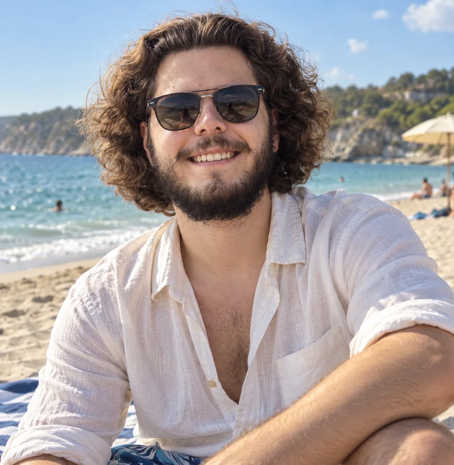 Mads-Bendt med solbriller på en strand med klippekyst i baggrunden.